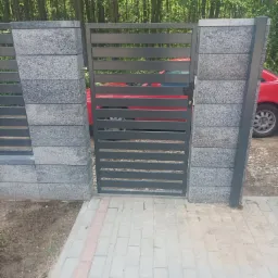 Nowoczesna brama wjazdowa z poziomymi szczeblami, osadzona w słupkach z szarego, strukturalnego betonu, z widocznym czerwonym samochodem w tle i kostką brukową na podjeździe.