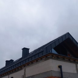 BLACHARSTWO-DEKARSTWO DARIUSZ KÓZKA - Nowoczesny dom w trakcie budowy, z ciemnoszarą blachą na dachu i widocznymi kominami na tle pochmurnego nieba.