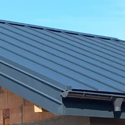 Nowoczesne, grafitowe krycie dachu z blachy na budynku w trakcie budowy, widoczne rynny i mur z pustaków.