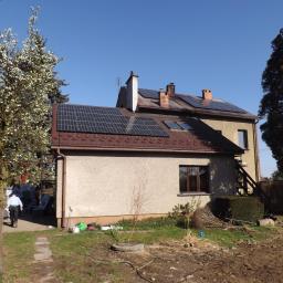 fasadapol - Dwukondygnacyjny dom z panelami słonecznymi na dachu, widok z ogrodu w słoneczny dzień, z widocznymi materiałami izolacyjnymi i pracownikiem w tle.