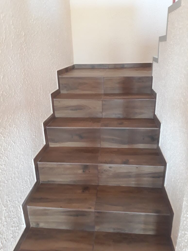 Schody wyłożone brązowymi płytkami imitującymi drewno, ściany w odcieniach bieli, widok z dołu.