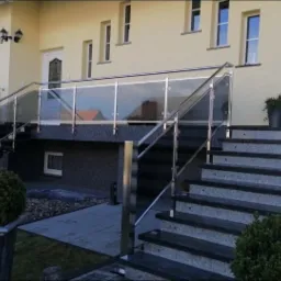 Zewnętrzne schody wejściowe do domu z grafitowymi stopniami i balustradą ze stali nierdzewnej z przezroczystym szkłem, widok z dołu.