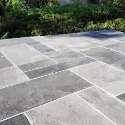 Fast Top Crete System - Ułożona z prostokątnych płyt w odcieniach szarości nawierzchnia tarasu, z zielenią w tle.