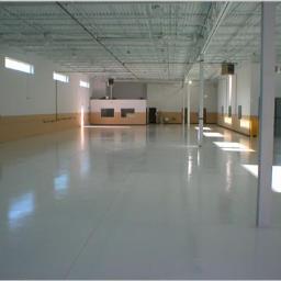 Fast Top Crete System - Biała, błyszcząca posadzka przemysłowa w dużej hali z widocznymi słupami i oknami w górnej części ścian.