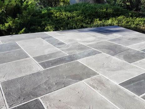 Ułożona z prostokątnych płyt w odcieniach szarości nawierzchnia tarasu, z zielenią w tle.
