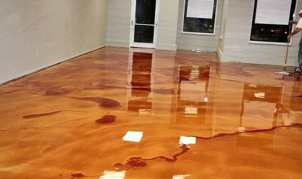 Błyszcząca, miedziana posadzka żywiczna z efektem marmuru w trakcie aplikacji, widoczne białe kartki zabezpieczające i pracownik rozprowadzający żywicę za pomocą narzędzia na długim kiju.