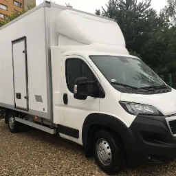 Biały Peugeot Boxer z zabudową kontenerową i rejestracją KR 5HA01, zaparkowany na żwirowym podłożu przed budynkiem mieszkalnym i zielenią.