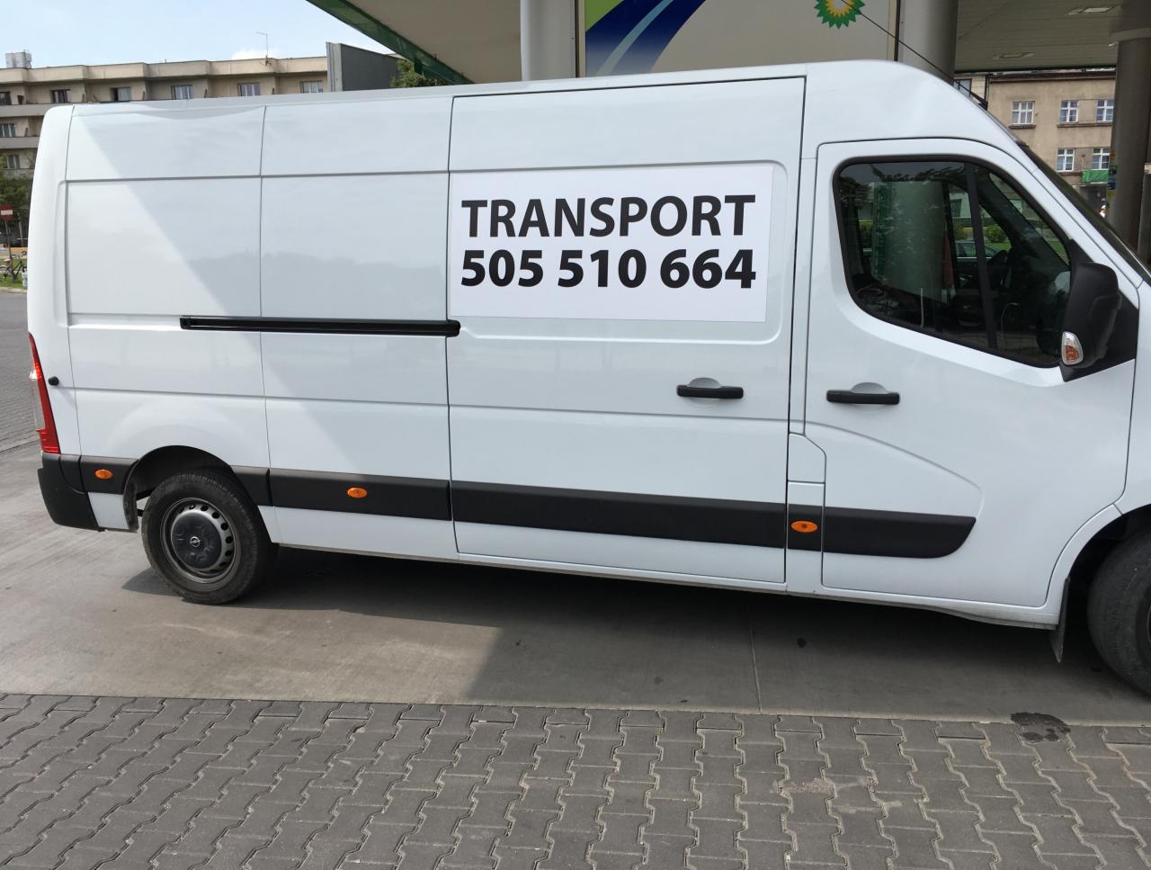 Biały bus transportowy z numerem telefonu zaparkowany przy stacji benzynowej w słoneczny dzień.