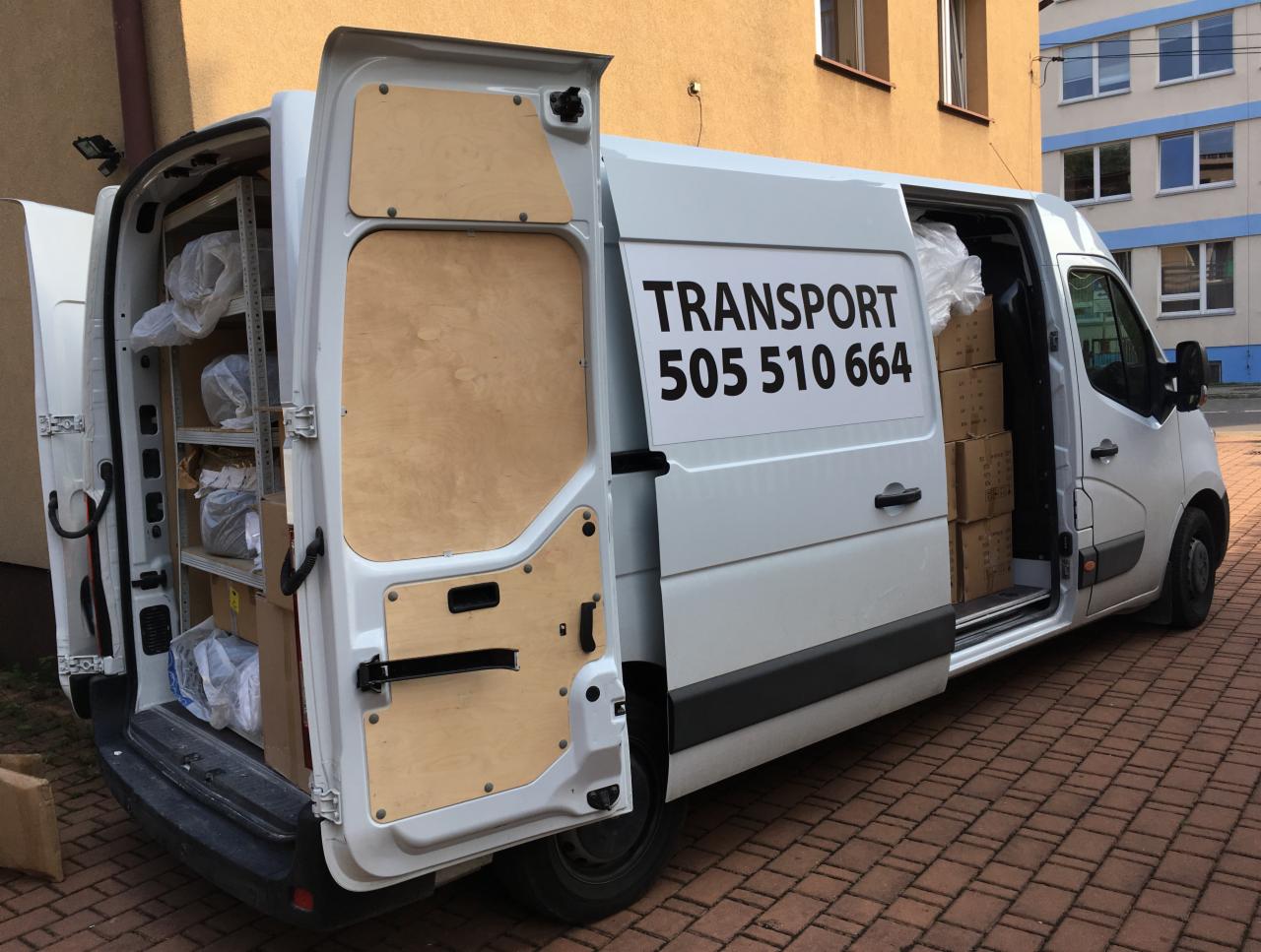 Biały van z otwartymi drzwiami, wypełniony kartonami i pakunkami, zaparkowany na chodniku z czerwonej kostki; na boku pojazdu napis 'TRANSPORT 505 510 664'.