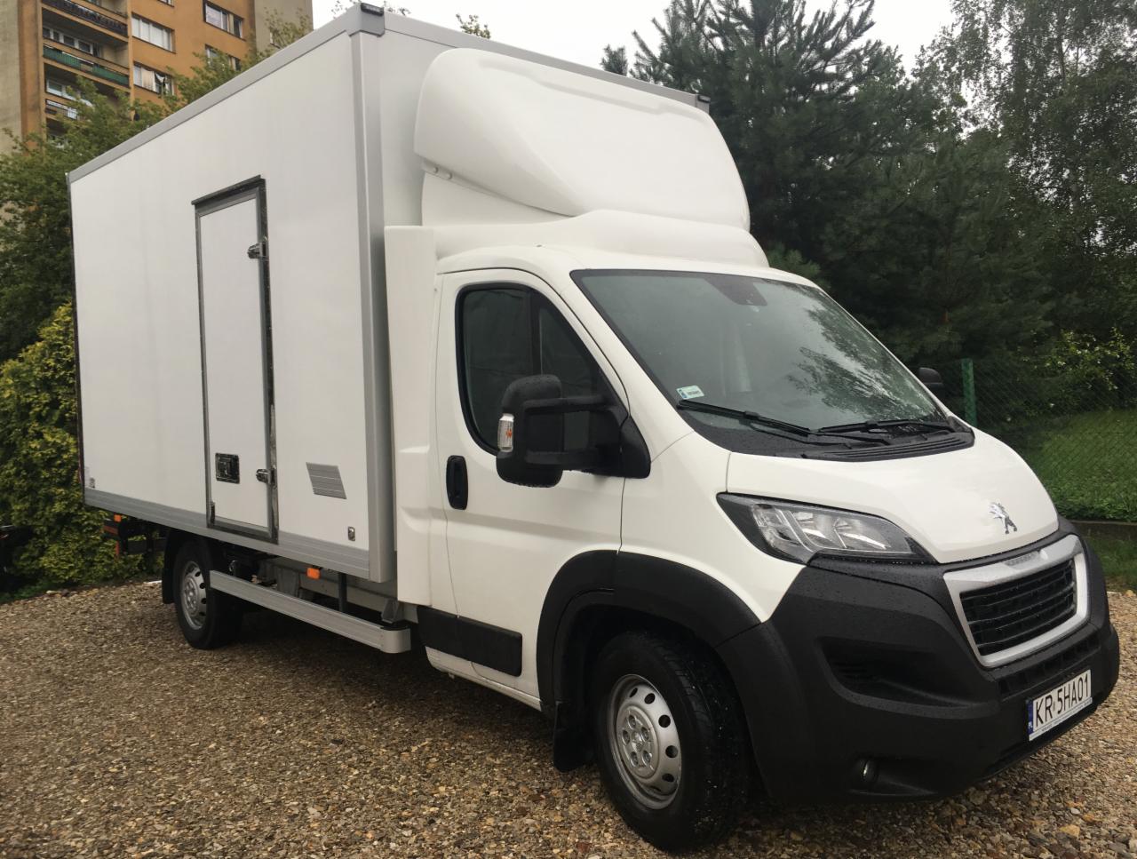 Biały Peugeot Boxer z zabudową kontenerową i rejestracją KR 5HA01, zaparkowany na żwirowym podłożu przed budynkiem mieszkalnym i zielenią.