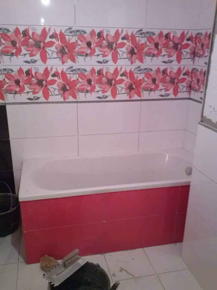 Wykończona wanna obudowana czerwoną glazurą, nad nią białe płytki z motywem kwiatowym, widoczny kubeł i kielnia glazurnicza.