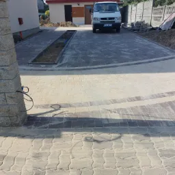 Ułożona kostka brukowa w dwóch odcieniach szarości tworząca wzór na podjeździe, z zaparkowanym białym vanem w tle.