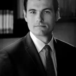 Portret biznesowy mężczyzny w garniturze, czarno-białe zdjęcie z książkami w tle.