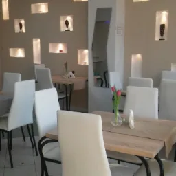 Wnętrze sali restauracyjnej w Głogowie z drewnianymi stolikami, białymi krzesłami, tulipanami w wazonach i dekoracyjnymi niszami w ścianie.