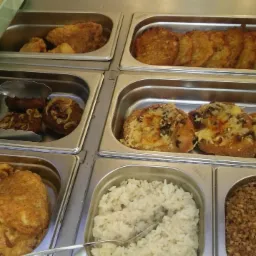 Bufet z różnorodnymi daniami: kotlety z cebulą, placki ziemniaczane, zapiekanki z serem, ryż biały i kasza gryczana, prezentowane w metalowych pojemnikach.