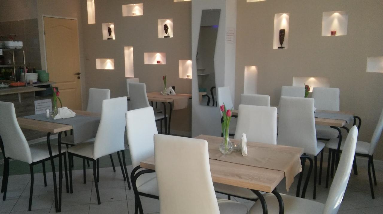 Wnętrze sali restauracyjnej w Głogowie z drewnianymi stolikami, białymi krzesłami, tulipanami w wazonach i dekoracyjnymi niszami w ścianie.