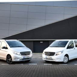Trans-Bus - Dwa busy Mercedes Vito, srebrny i biały, zaparkowane naprzeciwko nowoczesnego budynku z geometryczną fasadą.