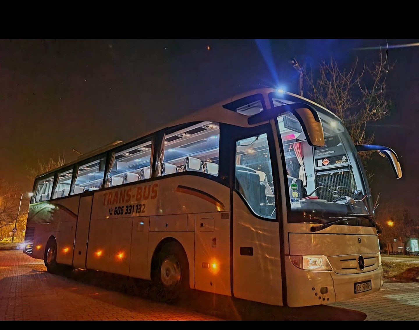 Autokar Mercedes-Benz Trans-Bus z widocznym numerem telefonu 606 331 132, sfotografowany nocą z włączonymi światłami pozycyjnymi.