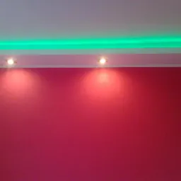 Czerwona ściana oświetlona dwoma punktowymi lampami i zielonym paskiem LED w suficie podwieszanym.