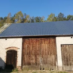 Częściowo pokryty, ciemnoszary dach z blachodachówki na budynku gospodarczym w Zielonej Górze, widoczne krokwie i rynna.