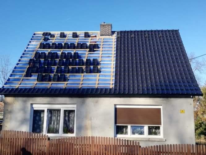 Dom jednorodzinny z częściowo zdjętym starym i częściowo ułożonym nowym, czarnym pokryciem dachowym. Widoczne drewniane łaty pod nowe dachówki i komin z cegły.