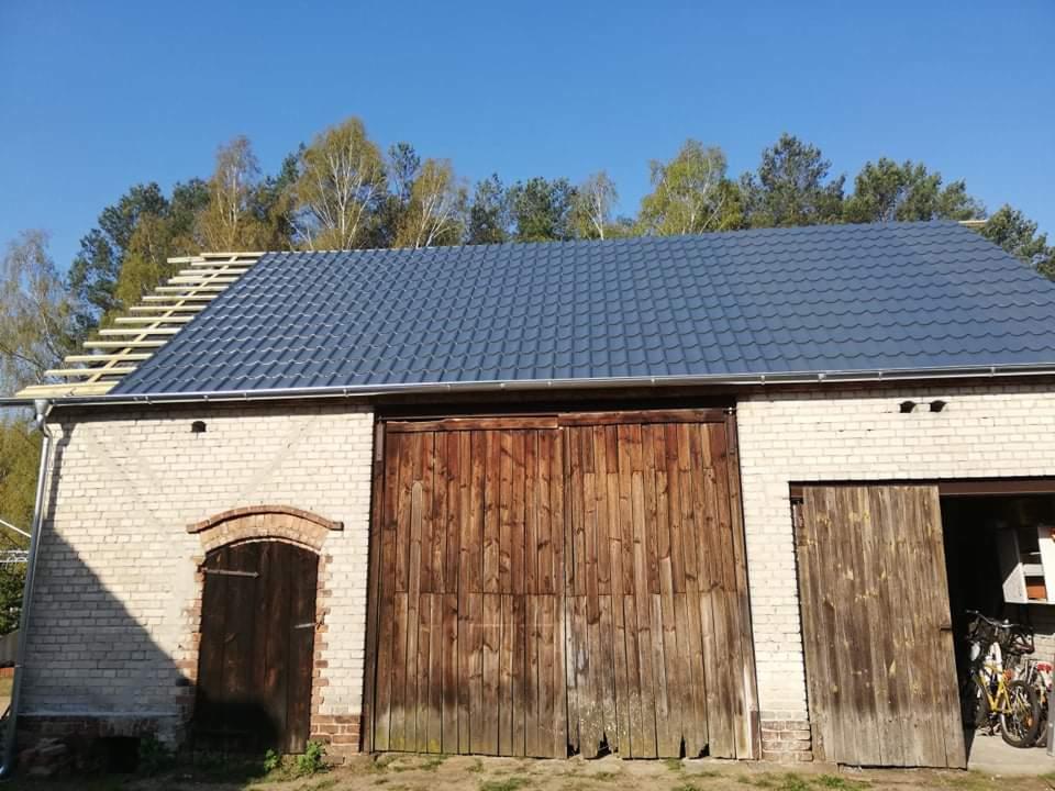 Częściowo pokryty, ciemnoszary dach z blachodachówki na budynku gospodarczym w Zielonej Górze, widoczne krokwie i rynna.