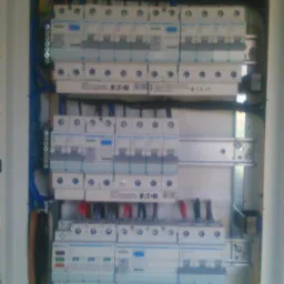Rozdzielnica elektryczna Eaton z zainstalowanymi bezpiecznikami i okablowaniem w kolorach niebieskim, żółtym, brązowym i czarnym, widoczna w białej obudowie.