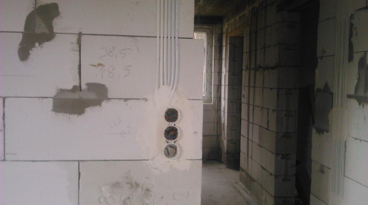 Instalacja elektryczna w surowym budynku: trzy puszki podtynkowe z przewodami w białych rurkach, ściany z betonu komórkowego z widocznymi śladami zaprawy i numerami naniesionymi odręcznie.