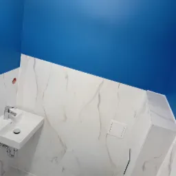 Wykończona łazienka z niebieską ścianą, białymi marmurkowymi płytkami, wiszącą umywalką i podwieszanym WC z zabudową.