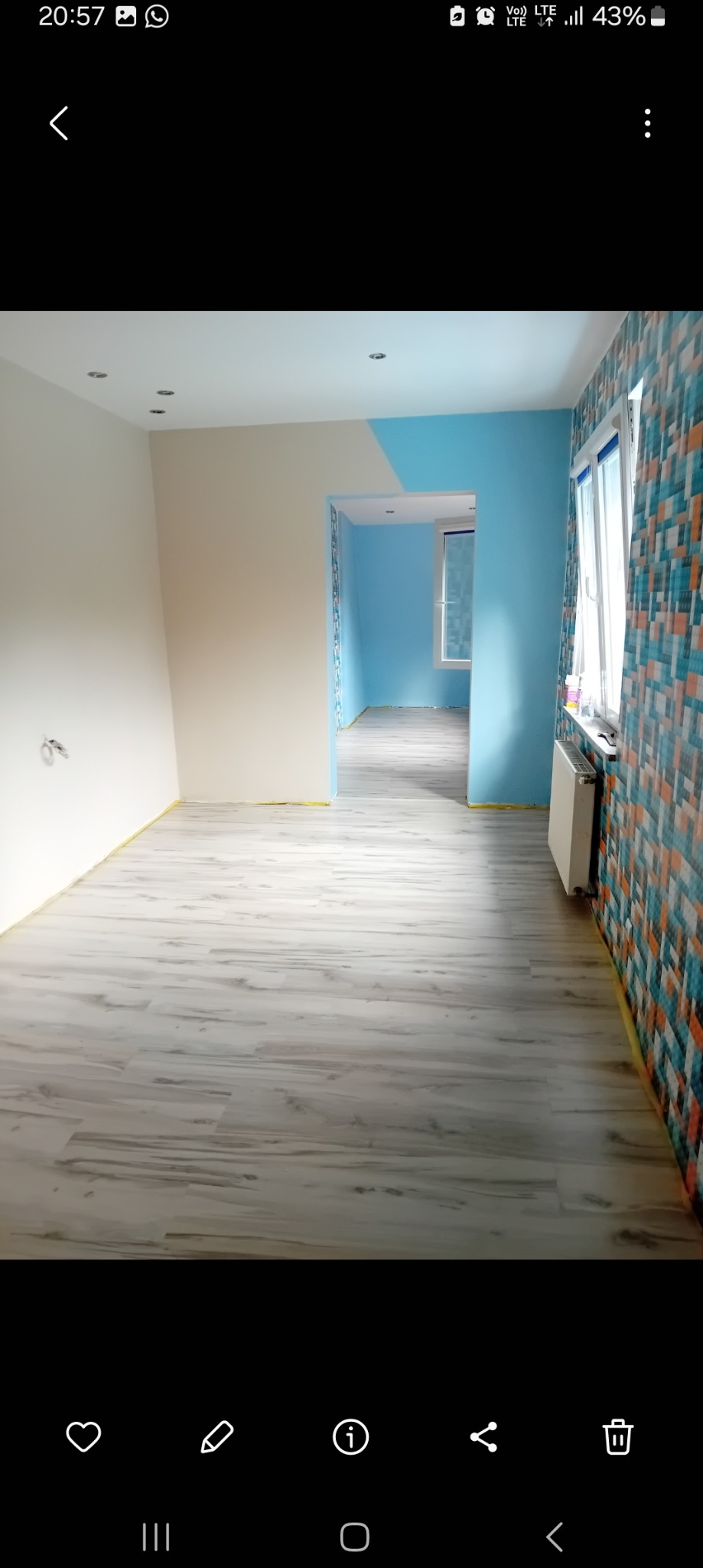 Wnętrze po odświeżeniu: jasne panele podłogowe, ściany częściowo pomalowane na biało i błękitno, z akcentem w postaci wzorzystej tapety na jednej ścianie, oklejone taśmą malarską przy podłodze.