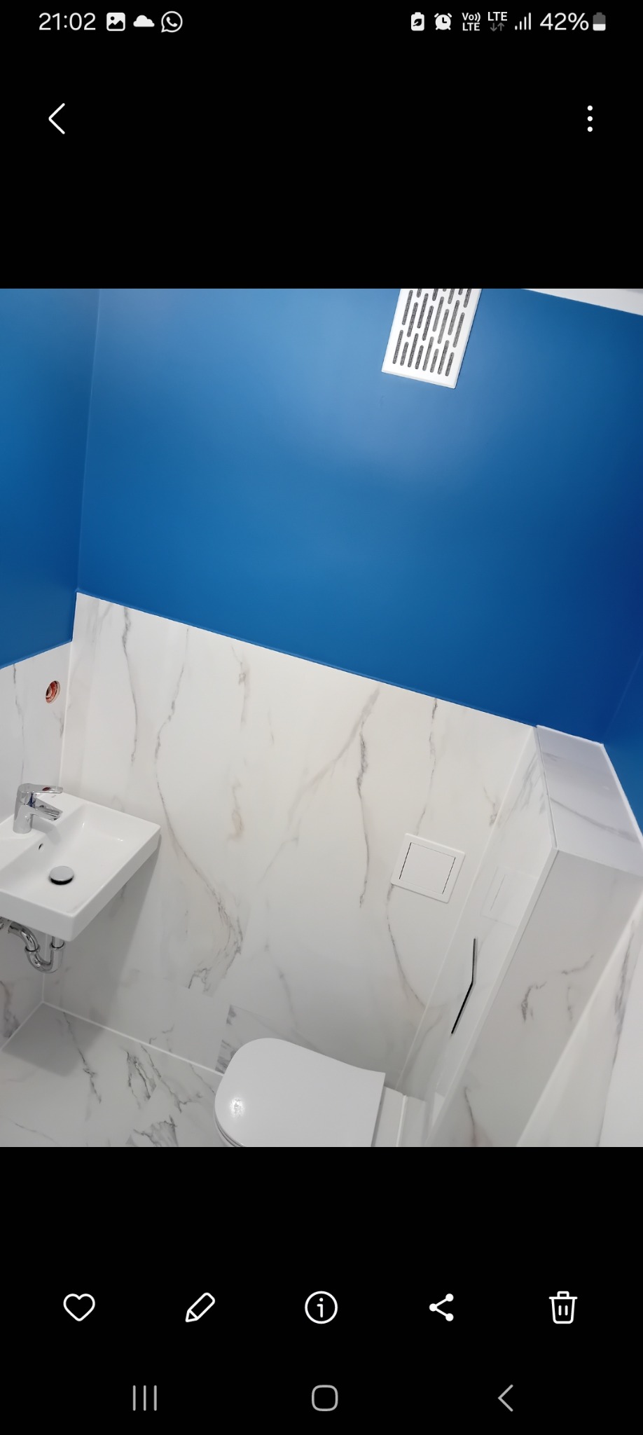 Wykończona łazienka z niebieską ścianą, białymi marmurkowymi płytkami, wiszącą umywalką i podwieszanym WC z zabudową.