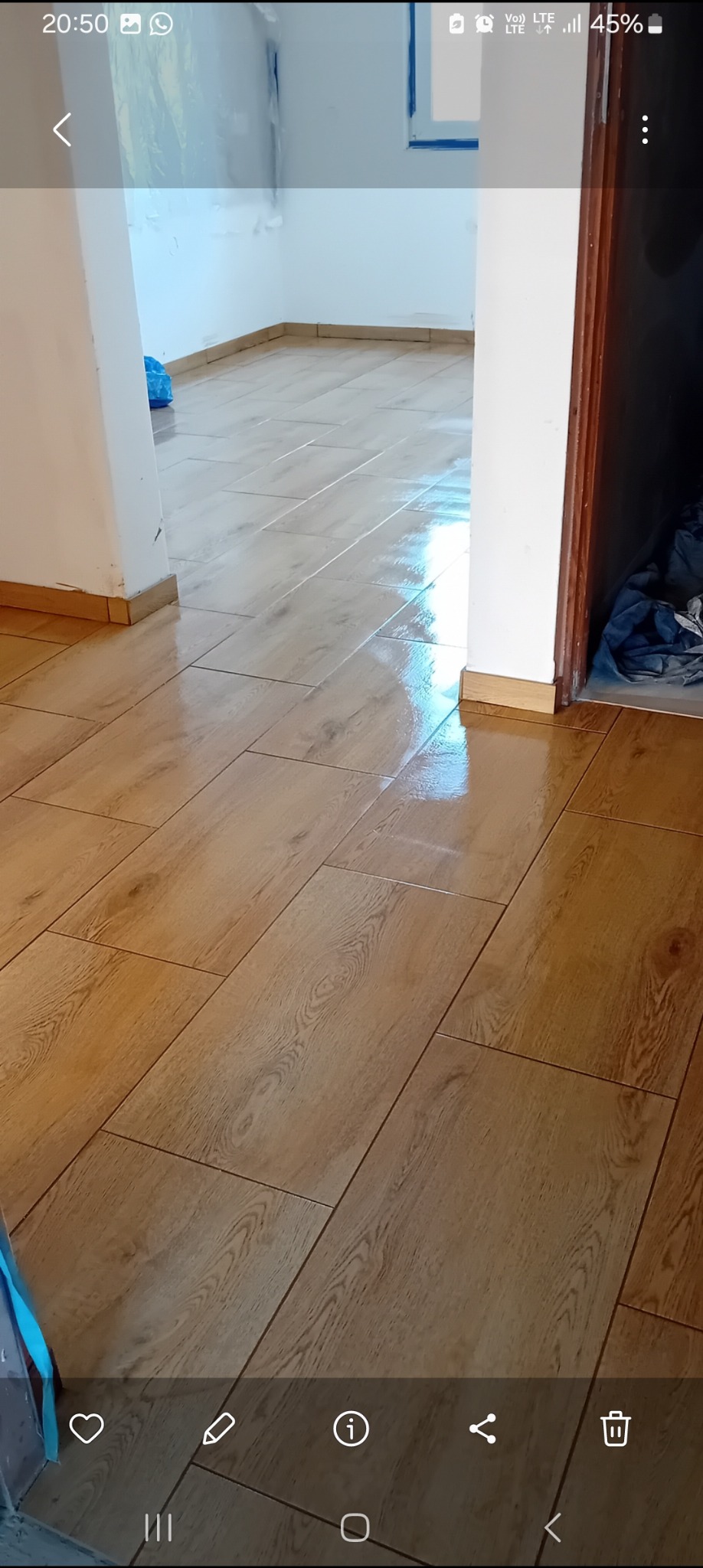 Połyskująca, świeżo położona podłoga z płytek imitujących drewno w korytarzu, widoczne łączenia płytek i listwy przypodłogowe.