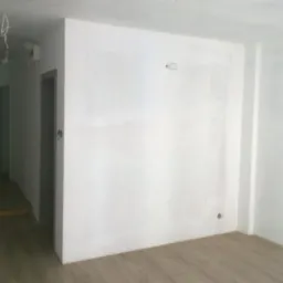 Wnętrze mieszkania po szpachlowaniu ścian, widoczne gładzie i przygotowane podłoże pod malowanie, panele podłogowe ułożone.