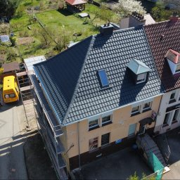 FACH BUD TOMASZ CHOMICZ - Budynek z częściowo wymienionym dachem, widoczne rusztowania i żółty bus firmy dekarskiej. Połowa dachu pokryta nową, grafitową dachówką, druga połowa ze starą, czerwoną.