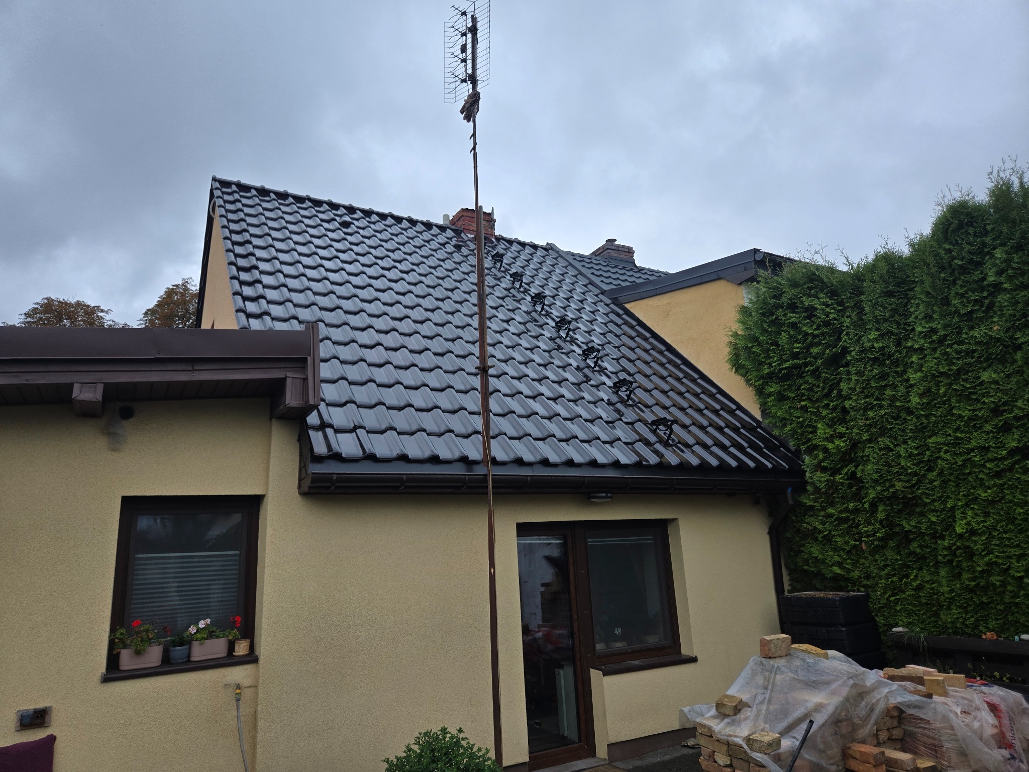 Czarny dach z anteną w Dębnie, widok z dołu. Nowe pokrycie dachowe na domu jednorodzinnym. Dachówka ceramiczna, ciemna kolorystyka, pochmurne niebo.