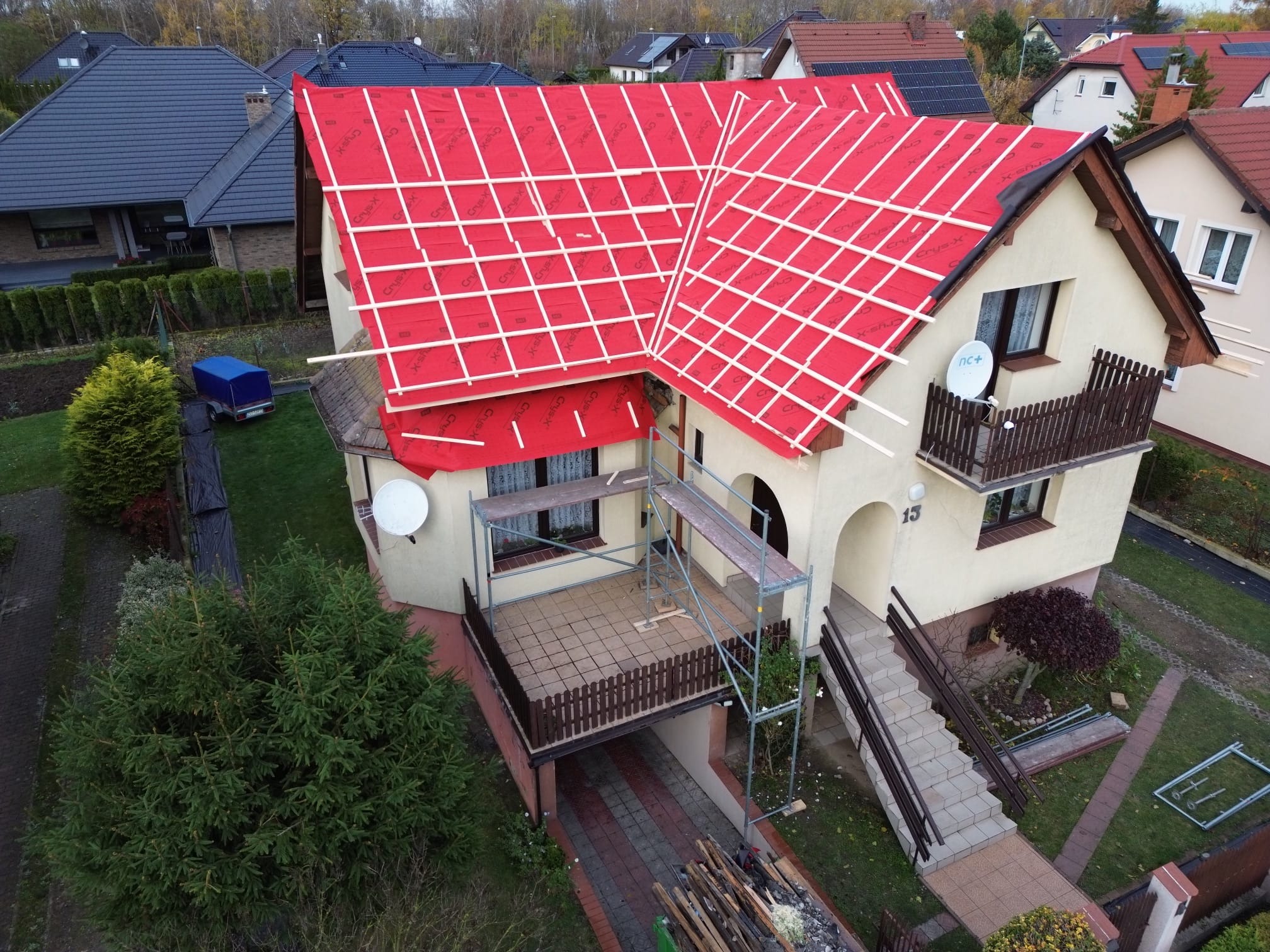 Dom z czerwonym pokryciem dachowym w trakcie montażu łat, widok z góry. Na dachu widoczne białe listwy. Częściowo widoczne rusztowanie.