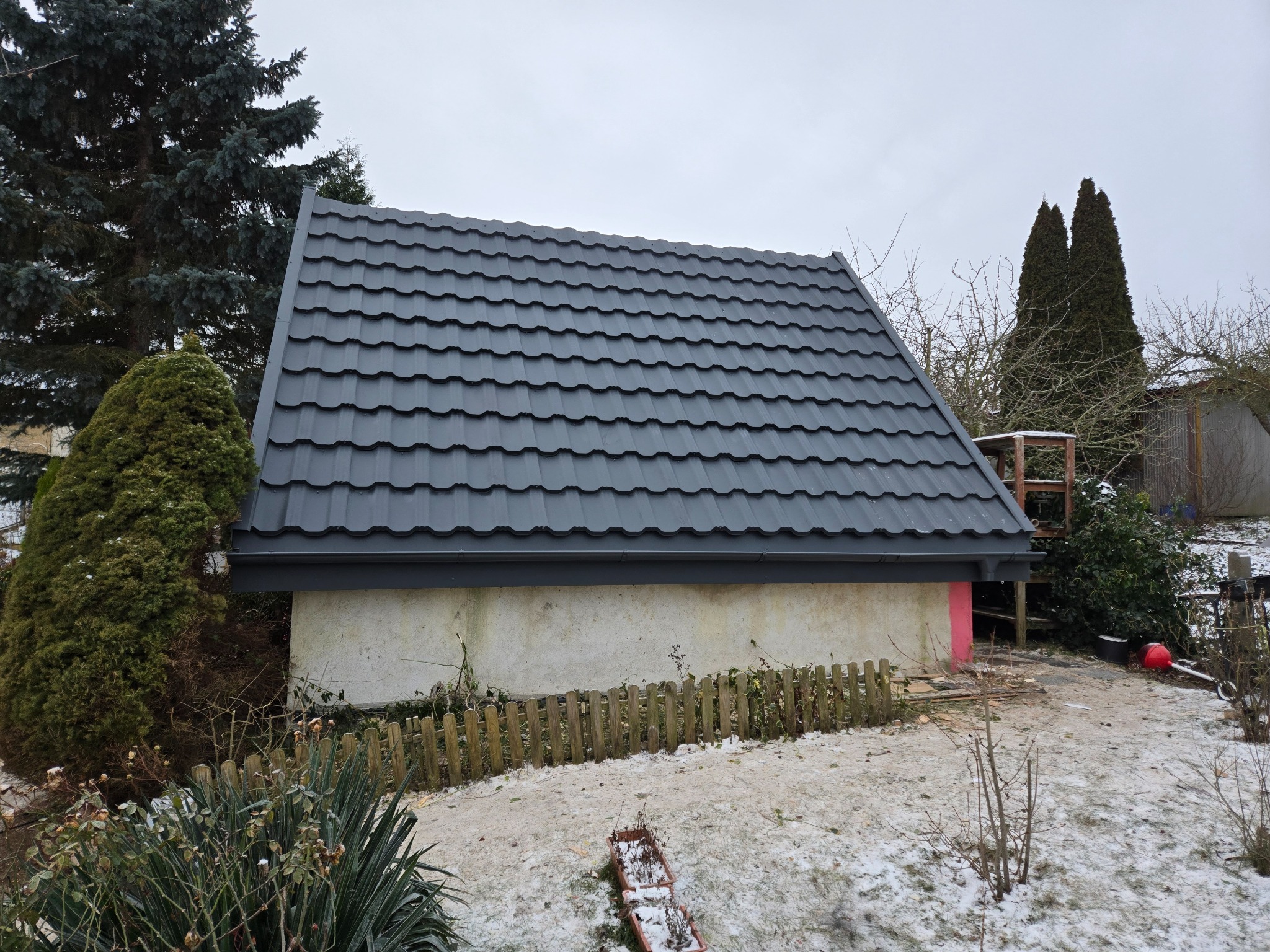 Dom z nowym, grafitowym dachem z blachodachówki modułowej, widoczny z poziomu gruntu w zimowej scenerii. Dach kontrastuje z jasną elewacją budynku.