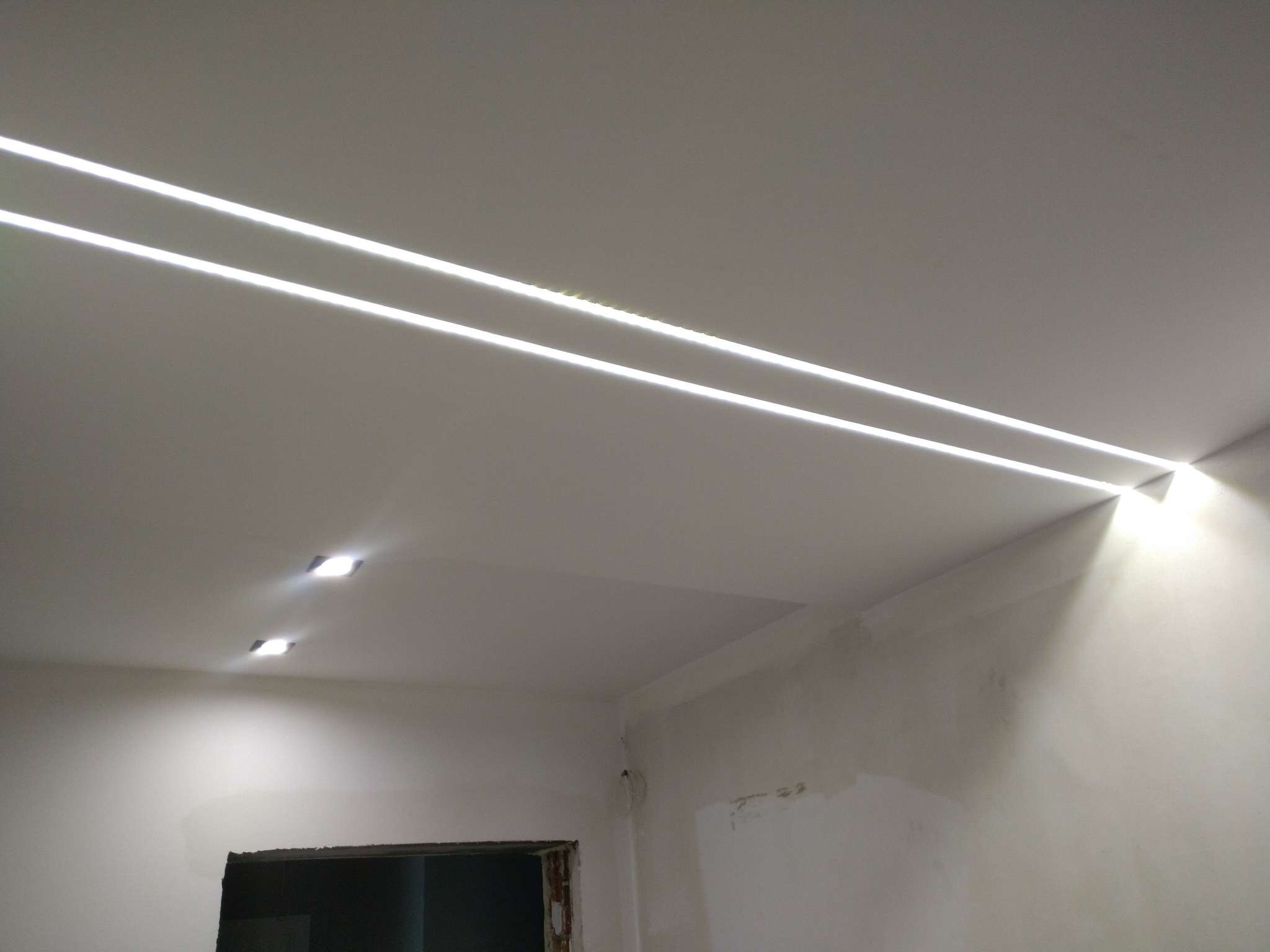 Dwa równoległe pasy oświetlenia LED w suficie podwieszanym, dodatkowe dwa punkty świetlne w suficie, ściany w trakcie wykańczania.