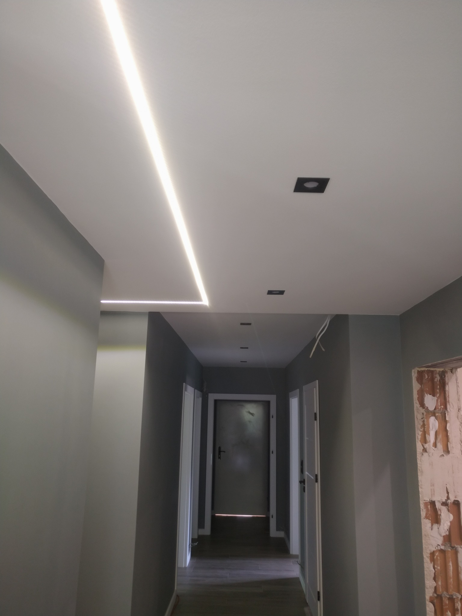 Korytarz z zamontowanym oświetleniem LED w suficie i punktowymi lampami. Na ścianie widoczne ślady po remoncie.