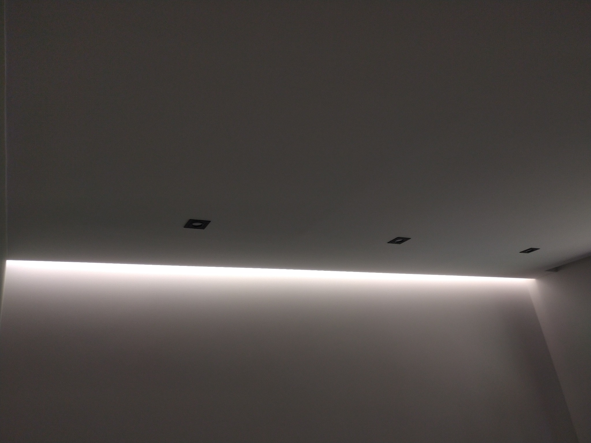 Minimalistyczne wnętrze z ukrytym oświetleniem LED w suficie i trzema małymi, kwadratowymi punktami świetlnymi