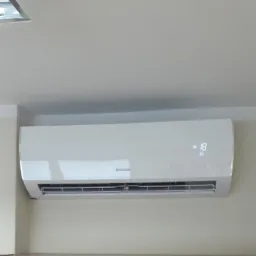 Biała jednostka klimatyzacyjna Sinclair zamontowana na ścianie nad szafkami, wyświetlająca temperaturę 18 stopni.