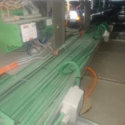 Sufit podwieszany z ułożonymi równolegle wiązkami zielonych kabli w peszlach, widoczne skrzynki przyłączeniowe i fragmenty instalacji sterowniczej.