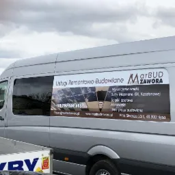 Srebrny bus firmy Marbud Zawora z reklamą usług remontowo-budowlanych, w tym wykończenia wnętrz, sufitów, ścianek działowych i malowania, zaparkowany na zewnątrz w pochmurny dzień.