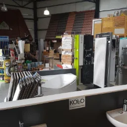 Wnętrze sklepu budowlanego z ekspozycją wanien, umywalek i paneli dachowych pod metalową konstrukcją dachu.