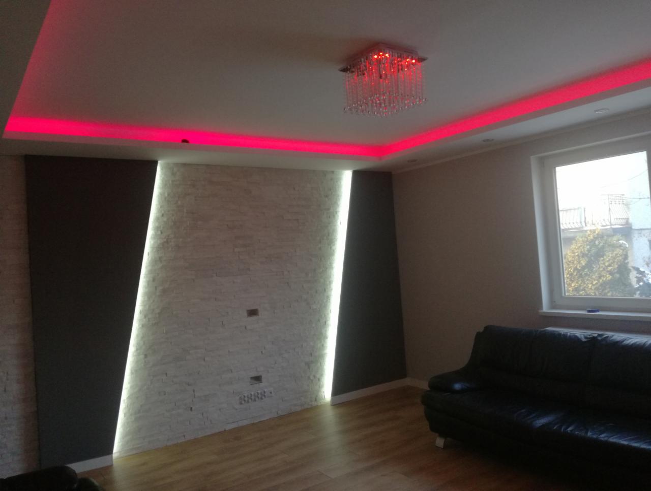 Salon z podświetlanym sufitem w kolorze czerwonym, dekoracyjną ścianą z białej cegły i czarnymi panelami, oświetleniem LED oraz kryształowym żyrandolem.