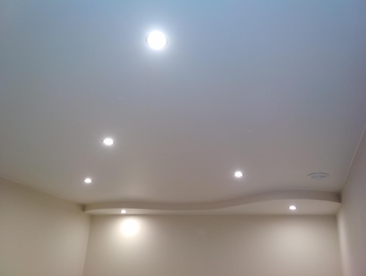 Gładki, biały sufit podwieszany z wbudowanymi punktowymi lampami LED i dekoracyjnym, falistym elementem pod sufitem