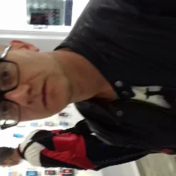 Portret mężczyzny w okularach i czarnej kurtce na tle ściany z ekranami w Świebodzinie.