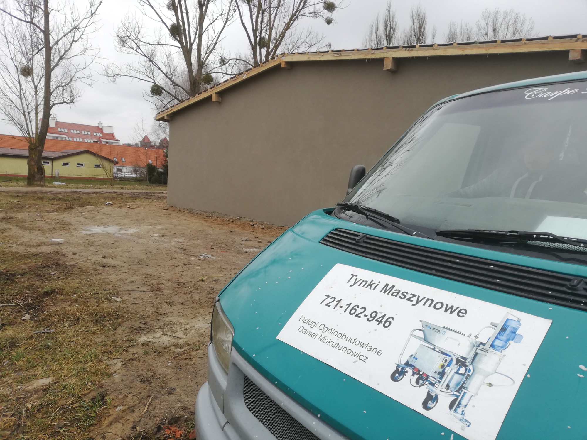 Świeżo otynkowana ściana budynku w tle, z przodu turkusowy samochód dostawczy z naklejką reklamową firmy oferującej usługi ogólnobudowlane, w tym numer telefonu i ilustrację maszyny do tynkowania.