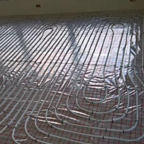 Białe rury ogrzewania podłogowego ułożone na folii odblaskowej z siatką, widok z góry pod kątem, przed wylaniem wylewki.