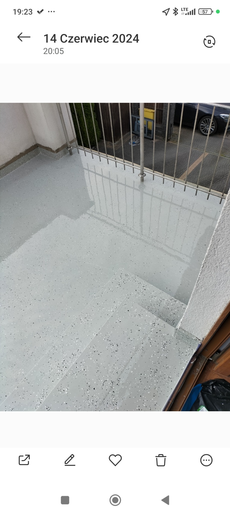 Jasnoszara, błyszcząca posadzka z drobnymi, czarnymi i białymi plamkami na balkonie z metalową balustradą, widoczne trzy stopnie schodów.